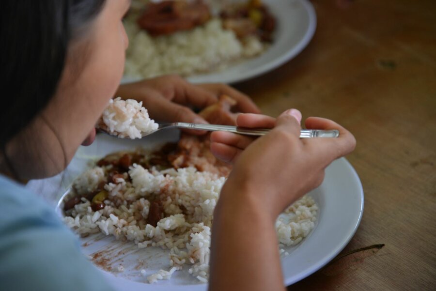 Una estudiante de primaria come un plato de arroz con frijoles.